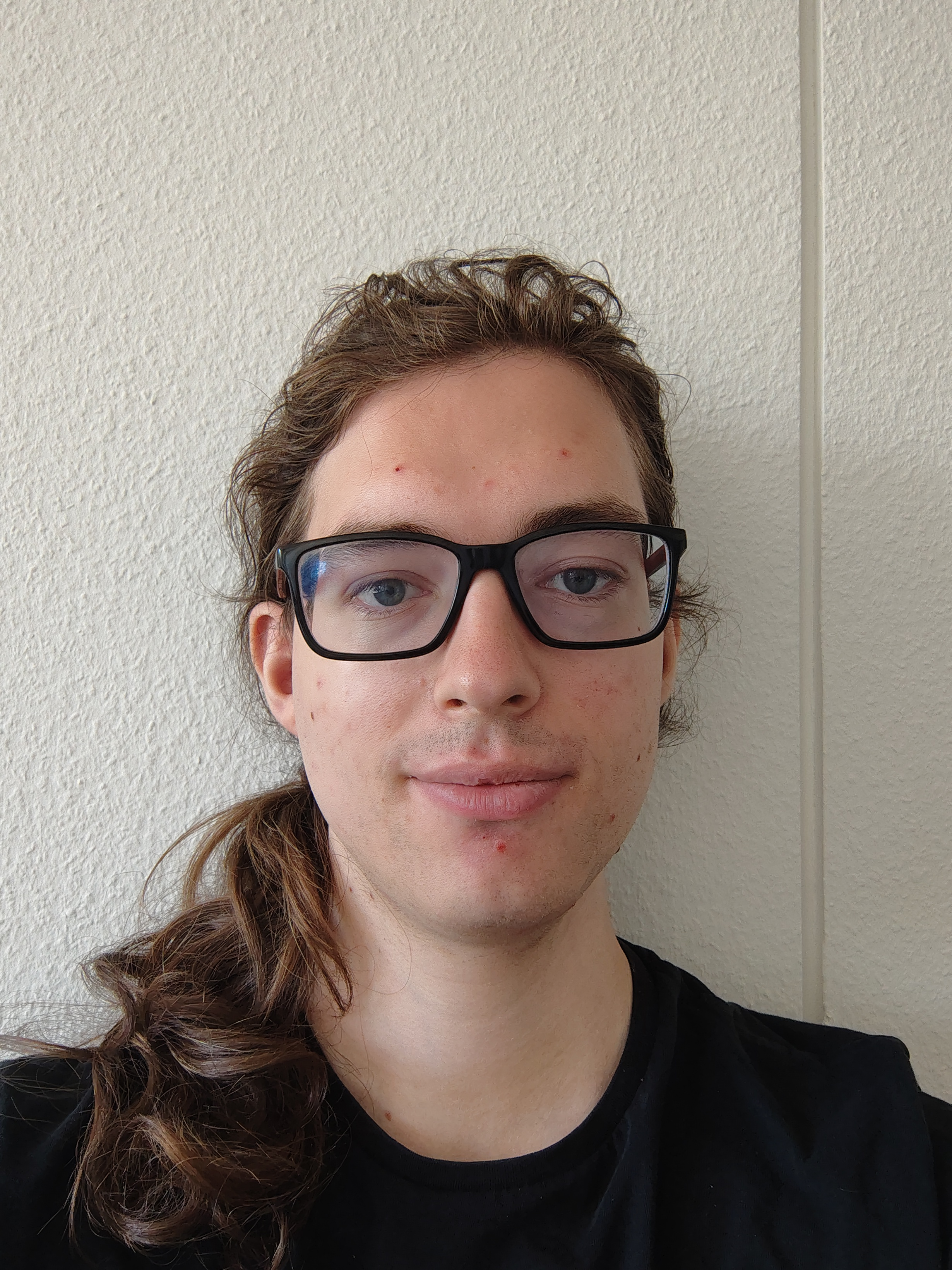 Porträtfoto fon Kate Jung: Professionelle Aufnahme vor weissem Hintergrund. Trägt ein schwarzes T-Shirt und hat schulterlange braune Haare